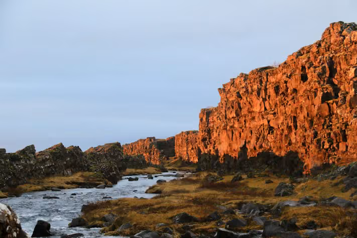 Rock walls of the rift valley at Þingvellir glowing in evening light beside a river
